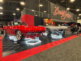Two classic corvettes, one red one silver, resting on MaxRamps wheel cradles at Barrett-Jackson car auction.
