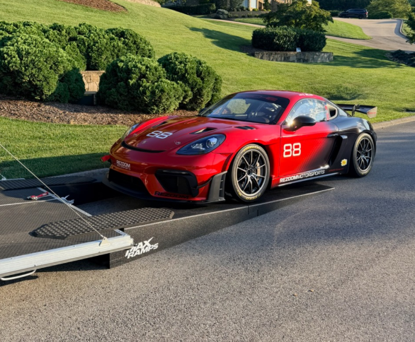 Red Porsche sports car drive up MaxRamps car hauler ramps and going into a trailer with a background of lush grass and greenery.