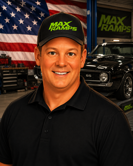 A smiling man in a black polo shirt and black cap with green 'MAX RAMPS' text stands in a garage-like setting with an American flag, a black classic car, and a large MAX RAMPS sign in the background.
