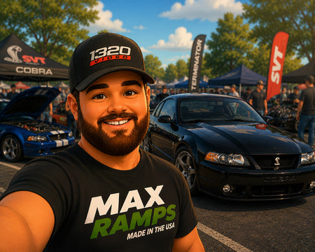 A smiling man in a black t-shirt and cap takes a selfie at an outdoor car show. The t-shirt features the text 'MAX RAMPS MADE IN THE USA' in white and green