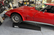 A red classic Corvette parked in a garage on a black MaxRamps drive-up ramp, with shelves and tools visible in the background.